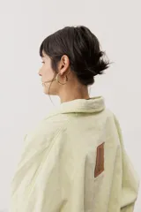 Chaqueta oversize de gabardina color verde claro, con solapa clásica, bolsillos frontales, cierre de botones oscuros y mangas largas con vuelta en tono verde lima vibrante.
