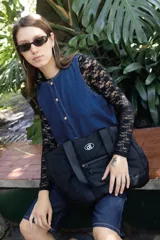 Bolso tipo tote de diseño urbano, confeccionado en material impermeable acolchado de color negro. Cuenta con doble asa de hombro, compartimento principal con cierre, bolsillo frontal con cierre y detalle de logo circular en la parte superior.