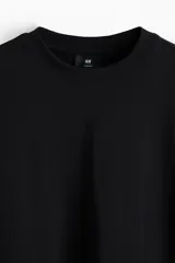 Remera negra de manga larga en punto de algodón de peso medio, con cuello redondo acanalado, hombros caídos, puños acanalados y bajo recto. Presenta un corte holgado.