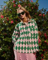 Camisa de corte holgado con cuello solapa y cierre frontal abotonado. Presenta un estampado geométrico de rombos en colores verde y rosado, con un bolsillo frontal en el pecho.