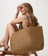 Cartera tipo tote de papel trenzado color marrón, con asas de hombro y detalle metálico dorado en el frente. Incluye neceser interno.