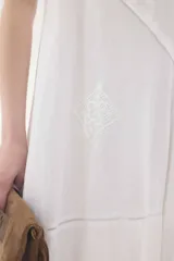 Vestido midi de lino color salmón, de corte amplio y silueta holgada. Presenta diseño con cortes irregulares y detalles de pasamanería en el escote y costuras. Cuenta con breteles dobles tipo cuerda y ruedo asimétrico.