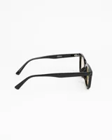 Lentes de sol de montura gruesa color negro, estilo cuadrado/rectangular. Poseen cristales tintados en color ámbar/beige claro. Presentan detalles metálicos (remaches) en las esquinas superiores del frente.