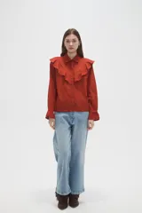 Camisa de algodón color terracota con cuello camisero, volados en el pecho y puños con detalle de encaje. Presenta cierre frontal con botones y un corte holgado.