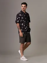 Camisa de manga corta Calvin Klein con corte relaxed fit, confeccionada en algodón regenerativo. Presenta un estampado floral en tonos blanco y gris sobre fondo negro, cierre frontal con botones y un bolsillo de parche en el pecho con el logo de la marca bordado.