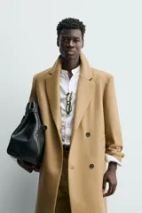 Abrigo largo color camel, de corte relajado (relaxed fit), confeccionado en tejido con mezcla de lana. Presenta cuello con solapas de muesca, manga larga, bolsillos de vivo en cadera, bolsillo interior y cierre frontal de botonadura cruzada.