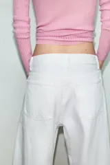 Jeans blancos de tiro medio con cinco bolsillos, detalle de costuras torcidas y cierre frontal con cremallera y botón metálico.