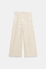 Pantalón de tiro medio confeccionado en hilatura con lino, con cintura con trabillas, bolsillos laterales ocultos y pierna ancha. Presenta un diseño con estampado jacquard de motivos florales en tonos beige y crudo, y cierre frontal con cremallera, botón y ganchos metálicos.