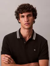 Chomba de piqué Calvin Klein color negro, con cuello clásico y ribetes a rayas blancas, cartera de dos botones y pequeño monograma CK bordado en el pecho.
