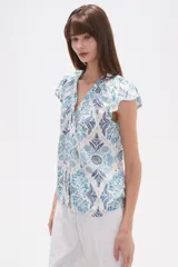 Blusa de rayón con estampado floral en tonos azules y celestes sobre fondo blanco. Presenta cuello en V, botones frontales y mangas cortas con frunces en los hombros.