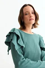 Remera de manga larga en color crudo, confeccionada en tejido acanalado, con detalle de volados en los hombros y cuello redondo.