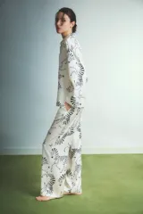 Pijama de dos piezas compuesto por camisa de manga larga con botones y pantalón recto, confeccionado en tela satinada color crema con estampado de cebras en negro.