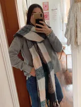 Bufanda amplia y abrigada con diseño de cuadros en tonos gris, beige, marrón y azul, terminada con flecos en los extremos.