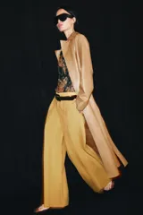 Jeans de tiro bajo y corte wide leg, color amarillo mostaza, con pliegues frontales, bolsillos ocultos y cierre frontal con cremallera, botón y ganchos metálicos.