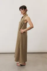 Vestido largo color marrón, sin mangas y con escote halter. Cuenta con bolsillos laterales y corte holgado.