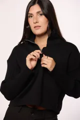 Buzo tejido de punto color negro, con cuello alto y cierre frontal parcial. Presenta mangas largas con textura acanalada tipo morley y corte holgado.