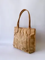 Bolso tipo tote de cuero color camel, con costuras a la vista y tiras de ajuste laterales.