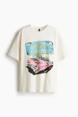 Remera de algodón color crema con corte oversized, cuello redondo y mangas cortas con hombros caídos. Presenta un estampado frontal con diseño gráfico de un auto clásico y tipografía alusiva a Bruce Springsteen.
