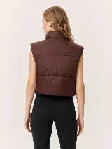 Chaleco puffer de corte cropped y diseño acolchado, con cuello alto y cierre frontal completo. Presenta un acabado liso en color marrón oscuro.