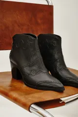 Bota corta estilo western de cuero vacuno negro, con puntera fina y detalles de textura grabada tipo reptil. Presenta costuras decorativas y apliques de tachas metálicas pequeñas en el diseño. Cuenta con taco cuadrado y cierre lateral.