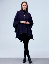 Ruana de tejido suave color azul marino, con corte asimétrico y ribetes de eco cuero negro en los bordes. Cierre frontal con tres botones dorados.