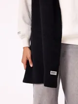 Bufanda de tejido de punto grueso en color negro, con etiqueta de la marca Rusty en uno de los extremos.