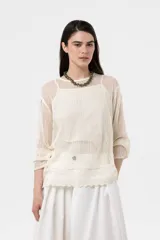 Sweater beige de punto abierto y liviano, con escote redondo, mangas largas y silueta amplia. Presenta detalle de broderie en el ruedo.