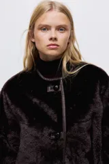 Chaqueta de textura suave efecto peludito en color marrón oscuro, con cuello redondo, cierre frontal mediante botones y bolsillos laterales ribeteados.