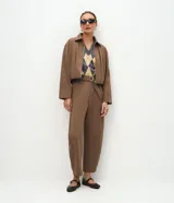 Pantalón de corte barrel, color marrón, confeccionado en algodón con felpa. Presenta cintura alta con cinto aplicado y hebilla metálica, y piernas de diseño amplio y cónico hacia los tobillos.