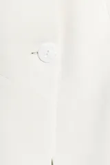 Blazer entallado color blanco de cuello sin solapa, manga larga con hombreras, falsos bolsillos delanteros de vivo y cierre frontal con un botón.