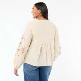 Blusa de color beige con cuello en V, mangas largas abullonadas con puños elásticos y bordados florales en el pecho y las mangas.