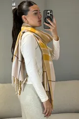Bufanda rectangular de tejido suave con diseño de cuadros escoceses en tonos mostaza, blanco y gris, terminada con flecos en los extremos.