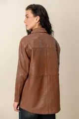 Campera estilo sobrecamisa confeccionada en cuero negro, de corte recto, con cuello camisero y cierre frontal de botones metálicos a presión.