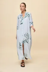 Vestido camisero largo de calce relajado, con patrón de rayas verticales celestes y blancas, y estampa floral en color verde. Posee cuello camisero, mangas largas y cierre frontal con botones.