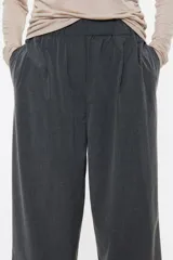 Pantalón negro de corte ancho y tiro alto, con cintura elástica fruncida y pliegues frontales.