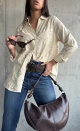 Camisa de color beige con diseño de broderie anglaise, cuello clásico, cierre frontal con botones y mangas largas.