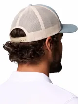 Gorra tipo trucker Columbia de color celeste con malla trasera en tono beige. Cuenta con un parche frontal bordado con diseño de montañas y el logo de la marca.