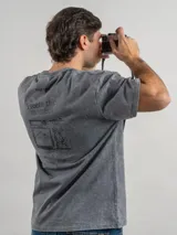 Remera oversize de algodón color negro con efecto lavado. Presenta un estampado gráfico en la espalda con la frase 'Freeze the moment' y un diseño de cámara fotográfica en tonos rojizos.