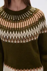 Sweater de poliéster color verde oliva con diseño geométrico en blanco, beige y marrón. Tiene cuello redondo, corte al cuerpo y detalles de cuentas en el cuello.