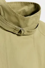 Cazadora de color verde militar, con cuello alto, manga larga abullonada con puños y cierre frontal con botones a presión ocultos. Incluye un cinturón ajustable del mismo tejido para entallar la cintura y bolsillos delanteros de vivo.