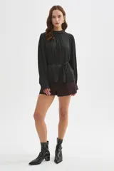 Blusa de poliéster color negro con cuello alto, mangas largas, diseño holgado, detalles de frunces y lazo ajustable en la cintura.