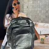 Mochila urbana de cuero sintético negro, con múltiples compartimentos frontales con cierre, bolsillos laterales y compartimento interno para notebook. Cuenta con correas ajustables y diseño funcional para uso diario.