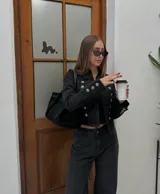 Campera estilo militar de color negro, con cuello mao y cierre frontal. Presenta múltiples botones metálicos plateados dispuestos en filas horizontales y detalles de charreteras en los hombros. Las mangas cuentan con puños decorados con botones a juego.