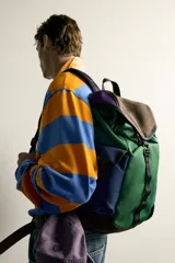 Mochila multibolsillos de diseño colorblock en tonos verde, azul marino, marrón y violeta, con solapa frontal y cierre de hebilla ajustable.