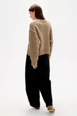 Sweater de punto canalé color beige, de corte holgado, con cuello redondo a la base y mangas largas con costuras decorativas.