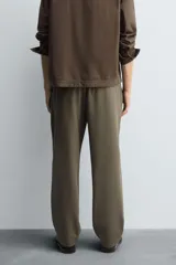 Pantalón regular fit color marrón oscuro, confeccionado en tejido con viscosa. Cuenta con cintura elástica, bolsillos delanteros y detalle de bolsillos traseros de vivo. El cierre frontal es con cremallera y botón.