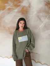 Sweater de hilo de algodón color tostado, con diseño tejido de la bandera de Uruguay en el frente, de manga larga y calce holgado.