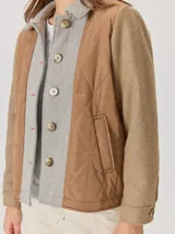 Campera de diseño híbrido con frente acolchado en color tostado, solapas y cuello en tejido de lana con patrón de cuadros tipo príncipe de gales, y mangas en paño de lana color azul marino. Cuenta con cierre frontal de botones.