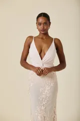 Vestido largo de fiesta con escote en V profundo y detalle de nudo en la cintura. La parte superior es de tela lisa y la falda presenta una superposición de tul con delicados bordados florales.