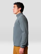 Buzo polar Mountain Hardwear modelo Microchill 1/4 Zip, color gris, con cuello alto, cierre frontal parcial de un cuarto y mangas raglán. Presenta detalles en color negro en los bordes del cuello, puños y ruedo, además de un pequeño logo bordado en el pecho.